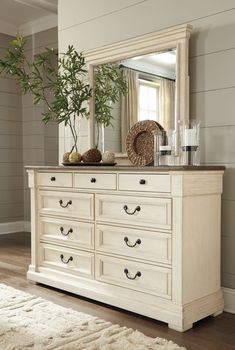 a white dresser with a mirror and vase on top of it in a living room