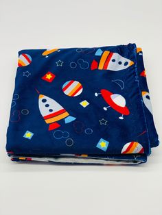 two pieces of blue fabric with colorful rockets and stars on the top, one is folded in