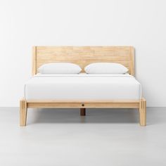 a bed with white sheets and pillows on top of it, against a white wall