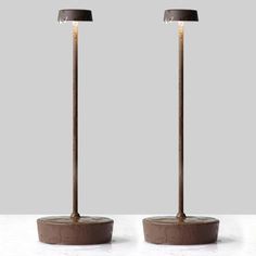 two floor lamps sitting next to each other on top of a white table with a gray background