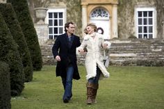 a man and woman are walking in front of a building with hedges on the lawn