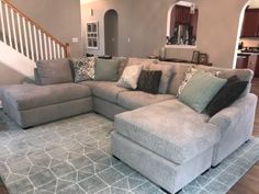 a large sectional couch with pillows on it in a living room next to an open staircase