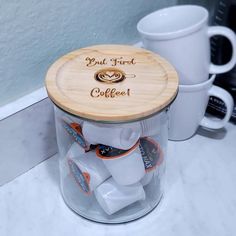 there is a glass jar with some coffee in it on the counter next to two mugs