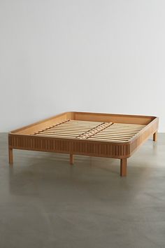 a wooden bed frame sitting on top of a cement floor next to a white wall