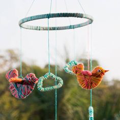 two colorful birds hanging from strings in front of trees