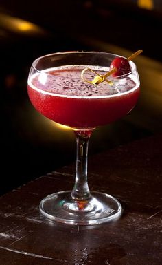 a red drink in a wine glass with an olive garnish on the rim