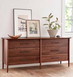 a wooden dresser with two pictures on the top and one potted plant sitting on top