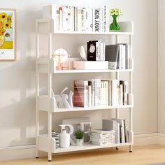 a white book shelf filled with books next to a vase and other items on top of it