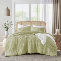 a bed with green comforter and pillows in a room next to a window filled with curtains