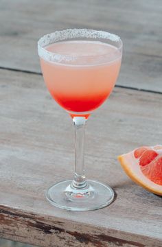 a grapefruit cocktail sitting on top of a wooden table next to a slice of grapefruit