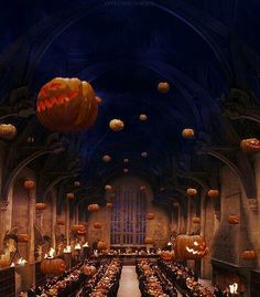 a large hall filled with lots of tables covered in pumpkins and lit up by candles