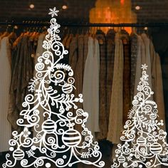 two white christmas trees are on display in front of some clothes hanging from the rack