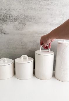 three white canisters with one holding a hand