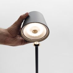 a hand holding a light on top of a black lamp post in front of a white wall