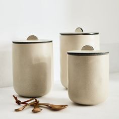 three white containers with black rims and spoons next to each other on a table