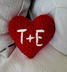 a red crocheted heart with the word te on it sitting on a bed