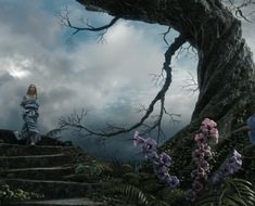 a woman is standing on some steps in the woods with flowers and trees around her