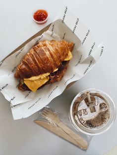 a croissant sandwich on top of a piece of paper next to a cup of coffee