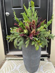 a large vase filled with lots of greenery sitting on top of a door mat