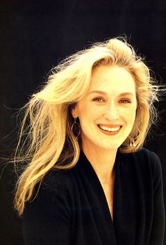 a woman with long blonde hair smiling at the camera while wearing a black cardigan