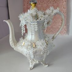 a silver tea pot with white flowers on the bottom and gold trimming around it