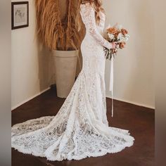 a woman in a long sleeved wedding dress standing next to a potted plant