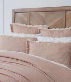 a bed with pink linens and white pillows on top of it, next to a wooden headboard