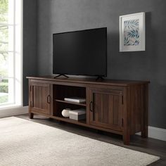 a flat screen tv sitting on top of a wooden entertainment center next to a window