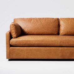 a brown leather couch with two pillows on the back and one arm folded over it