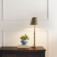 a table with a lamp, book and potted plant sitting on top of it