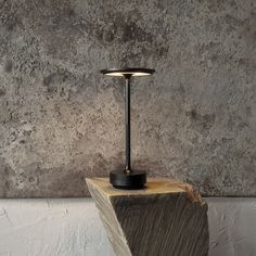 a lamp sitting on top of a piece of wood in front of a concrete wall