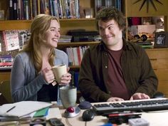 a man and woman sitting at a desk with a computer, keyboard, mouse and coffee cup