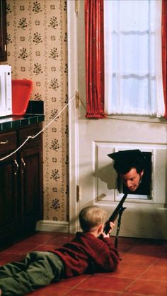 a young boy laying on the floor in front of a window with an umbrella over his head