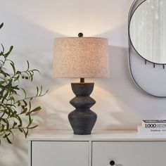 a table lamp sitting on top of a white dresser next to a mirror and potted plant