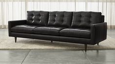 a black leather couch sitting on top of a rug in front of a white curtain