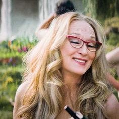 a woman with glasses is smiling and holding a wine glass in her hand while standing outside