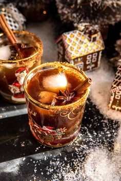 two glasses filled with hot chocolate and cinnamon on top of a table next to christmas decorations