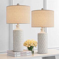 two white vases with yellow flowers sit on a table next to books and a lamp