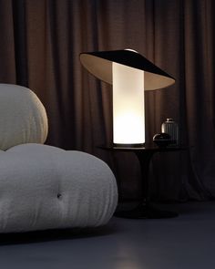 a lamp sitting on top of a table next to a white couch in front of a curtain