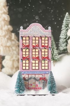 a pink toy store with christmas decorations on the windows and trees in the snow behind it