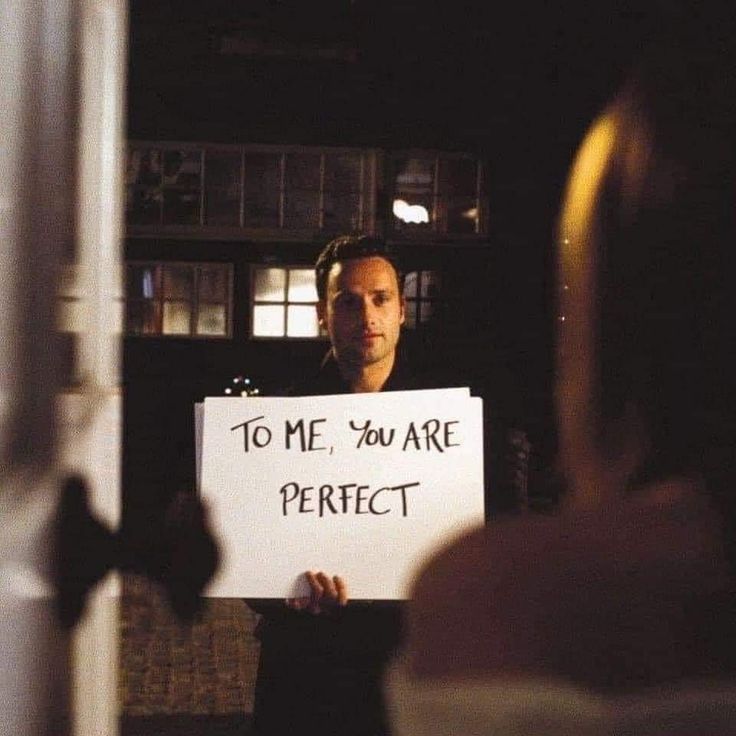 a man holding a sign that says to me, you are perfect in front of him