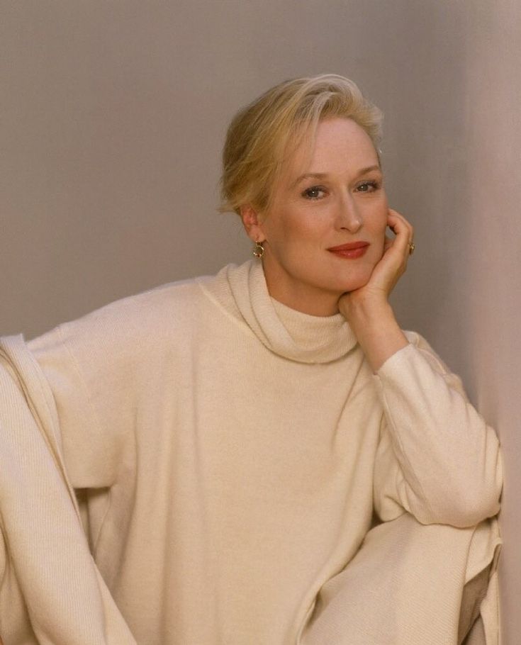 a woman with blonde hair wearing a white turtle neck sweater and sitting on a chair