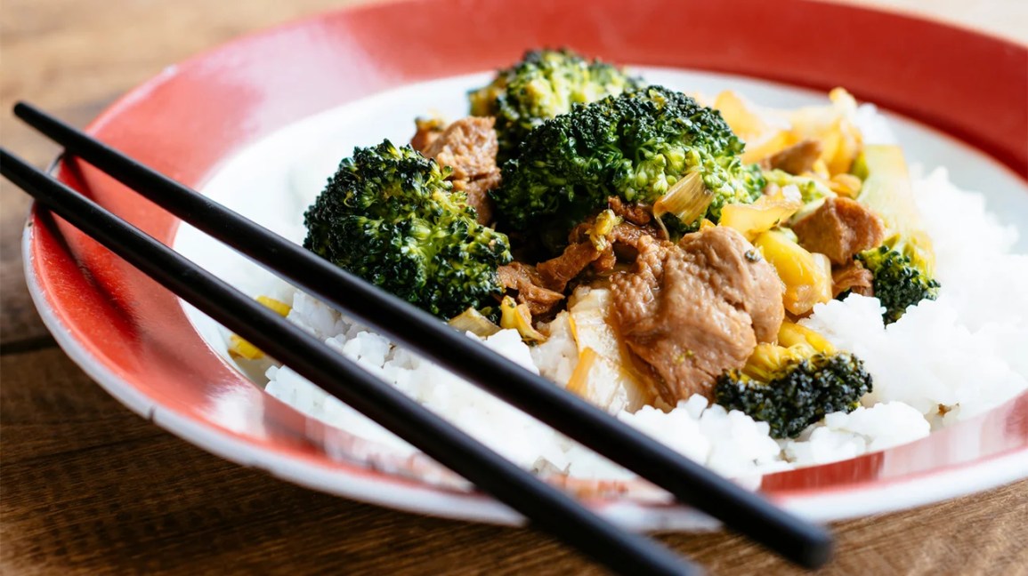 A plate of broccoli, vegan meat alternatives, and white rice with chopsticks.