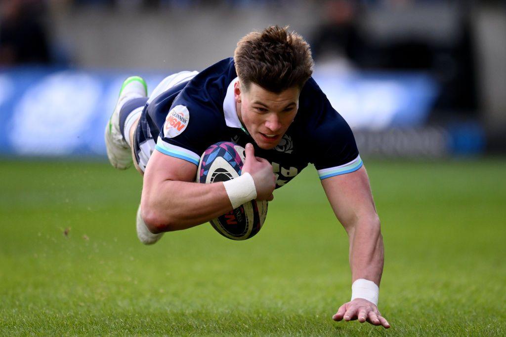 A man diving to score a try on a rugby pitch