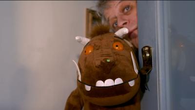 Gruffalo illustrator Axel Scheffler holds a stuffed Gruffalo toy around the side of a door