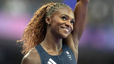 A smiling Dina Asher-Smith raises her left arm in a salute