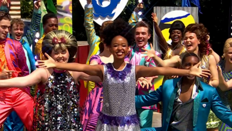 The cast of Hairspray the Musical in colourful clothes and wigs mid performance