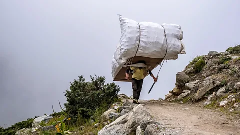 A sherpa carrying a huge load on his back on a track in Nepal (Credit: Getty Images)