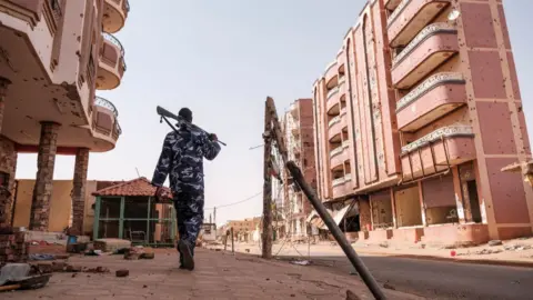 An armed policeman walks among damaged buildings in the area of the Souk, in the city of Omdurman.
