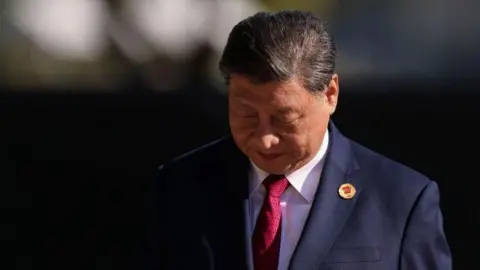 Xi Jinping in a navy suit and red tie looks down at the ground in a photo taken at the G20 Summit 2024 n November 18, 2024 in Rio de Janeiro, Brazil. 